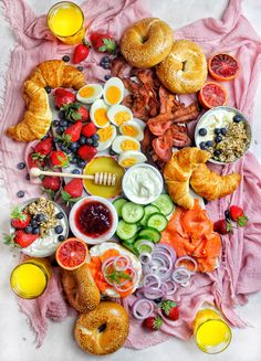 an assortment of food is laid out on a pink towel with orange juice and strawberries