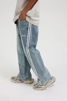 The Washed Striped Wide-Leg Pants seamlessly blend vintage style with contemporary craftsmanship. Featuring an all-over washed and distressed look, these pants are adorned with embroidered logos on each hip. The striking contrast stripes run from the back waist down the front of the legs, enhancing the body’s natural silhouette. Functional front pockets are decorated with rivets, while two back pockets provide additional utility. Crafted from premium fabric, these slightly oversized pants offer Casual Cotton Bottoms With Contrast Stitching, Faded Mid-rise Pants For Streetwear, Distressed Cotton Denim Blue Pants, Distressed Denim Blue Cotton Pants, Trendy Faded Cotton Pants, Sporty Wide Leg Cotton Jeans, Distressed Wide Leg Cotton Bottoms, Casual Denim Bottoms With Contrast Stitching, Casual Bottoms With Contrast Stitching And Straight Hem