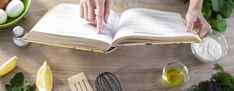 a person is reading a book on a table with ingredients and utensils around it