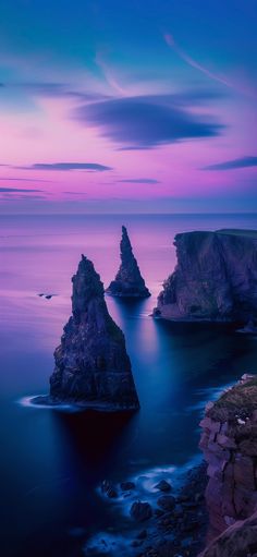 some very pretty rocks by the water at night time with purple and blue sky in the background