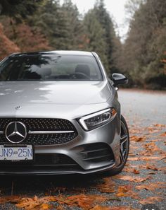 the front end of a silver mercedes cla parked on a road with leaves around it