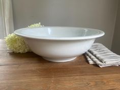 a white bowl sitting on top of a wooden table next to a napkin and flower