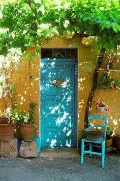 a blue door and chair in front of a yellow wall with potted plants on it