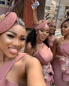 four women in pink dresses and hats taking a selfie