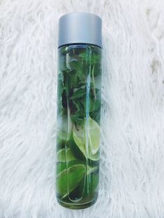 a water bottle filled with green leaves and limes on top of a white blanket