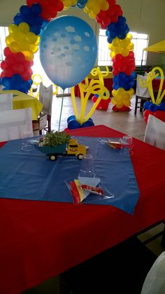 a red table topped with blue and yellow tables cloths covered in balloons, cars and kites