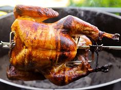 a roasting chicken is being cooked on an outdoor bbq grill with tongs