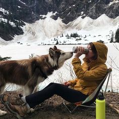 a woman sitting in a chair drinking from a bottle next to a dog