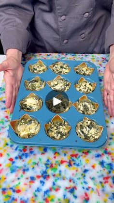 a person holding a tray with cupcakes in it on top of a table