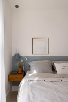 a bed with white sheets and pillows next to a wooden night stand in a bedroom