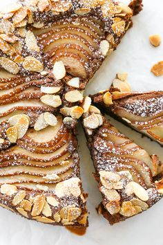 a sliced cake with almonds and powdered sugar on top, sitting on a white surface