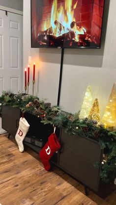 a flat screen tv sitting on top of a wooden table next to christmas stockings and candles