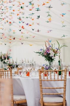 the table is set with wine glasses and paper cranes hanging from the ceiling above it