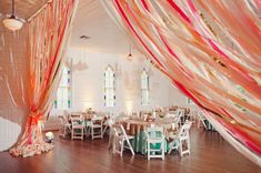 a banquet hall with tables and chairs covered in pink, white and gold ribbons hanging from the ceiling