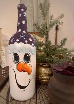 a wine bottle decorated with a snowman's hat and nose is sitting on a table next to a potted christmas tree