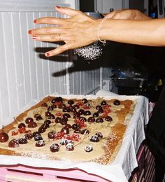 a woman reaching out her hand towards a cake with cherries on it and chocolates in the middle