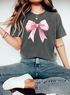 Embrace sweet elegance with our Pink Bow Coquette Tee, designed for those who love to add a touch of feminine charm to their style. Featuring a soft, delicate pink bow at the center, this coquette-inspired shirt is perfect for anyone who adores a blend of vintage glamour and modern flair. Made from soft, breathable fabric, it's both comfortable and stylish, perfect for casual outings or dressing up with your favorite accessories. Add a dash of playful sophistication to your wardrobe with this chic, must-have piece!" Product Features: - Soft Premium Quality Cotton - Available In Multiple Sizes And Colors - Unisex Fit Production Time: 1-2 Business Days Delivery Time: 2-5 Business Days Coquette Ribbon, Coquette Shirt, Shirt Coquette, Glamour Vintage, Bow Coquette, Bow Shirt, Pink Coquette, Bow Shirts, Mama T Shirt