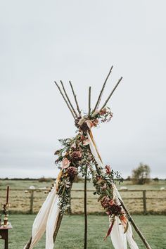 a teepee decorated with flowers and greenery for a wedding ceremony in the field