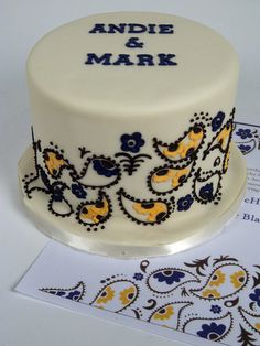 a white cake with blue and yellow designs on it sitting next to a note card