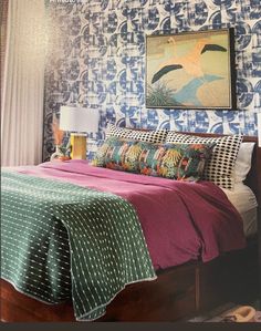 a bedroom with blue and white wallpaper has a large painting on the wall above the bed