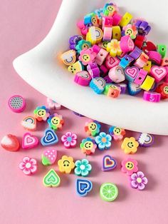 a white bowl filled with lots of different colored plastic beads next to a pile of cut up hearts and flowers