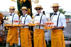 four men in yellow aprons holding wine glasses and champagne flutes at an outdoor event