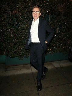 a man in a black suit and white shirt is walking down the street at night