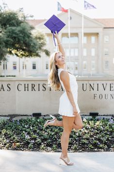 a woman in white dress holding up a purple graduation cap