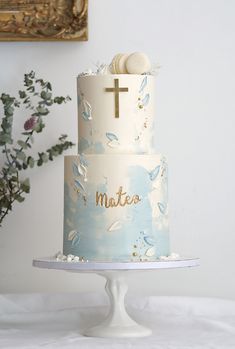 a blue and white cake with a cross on top is sitting on a table in front of a painting