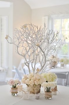 a white table topped with vases filled with flowers next to a tree and other decorations