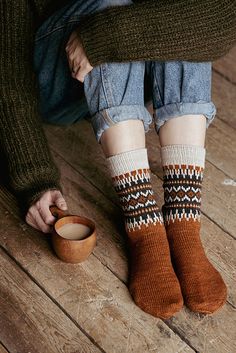 a person sitting on the floor with their feet up wearing socks and holding a cup