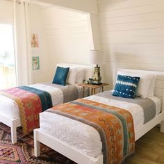 two beds in a room with white walls and wooden floors, one has a colorful blanket on the bed