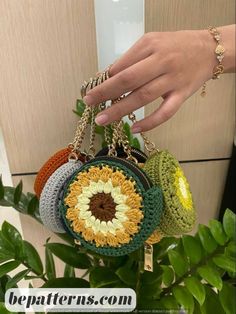 a hand holding four crocheted purses in front of a plant