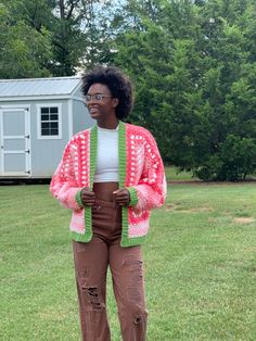 a woman standing in the grass wearing a pink and green knitted cardigan sweater