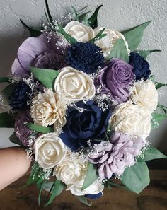 a bridal bouquet with purple, white and blue flowers on it is held by someone's hand