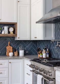 a kitchen with white cabinets and marble backsplash, stainless steel range hoods