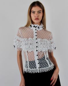 Introducing the elegant Alicia Blouse, crafted from Swiss Point D’Esprit with cotton lace ruffles, Venise trims, and satin baby bows. This soft, fitted blouse features an empire focus, adorned with delicate ruffles at the neckline and sleeves, complemented by satin pearl buttons at the center front. Available in White and Black or Black on Black. Swiss Point D’Esprit Cotton lace ruffles with Venise trims Satin pearl buttons Dry clean only Each piece is made to order and handcrafted in our atelie Designer Ruffled Summer Tops, Designer Ruffled Tops For Summer, Short Sleeve Lace Top With Ruffles, Elegant Summer Lace Top With Lace Cuffs, Designer Ruffled Tops For Evening, Designer Ruffle Tops For Evening, Elegant Short Sleeve Lace Blouse, Designer Evening Tops With Ruffles, Luxury Spring Tops With Ruffles