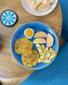 a blue plate topped with food on top of a wooden table next to a bowl of fruit