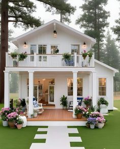 a white house with lots of plants and flowers on the porch