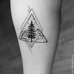 a black and white photo of a pine tree tattoo on the left calf leg, with mountains in the background