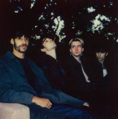 four men sitting next to each other in front of trees