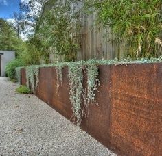 a long metal wall with plants growing on it's sides in front of a house