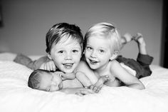 two young boys laying on top of a bed with their arms around each other and smiling