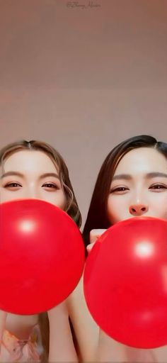 two women holding red balloons in front of their faces