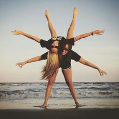 two young women are standing on the beach with their arms around each other as if they were doing a handstand