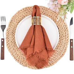 a place setting with an orange napkin, fork and knife on a wicker plate