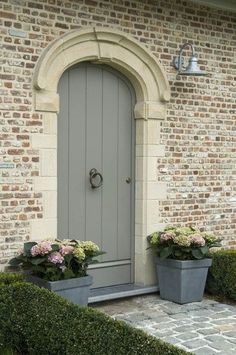 two planters with flowers are in front of a gray door on a brick building