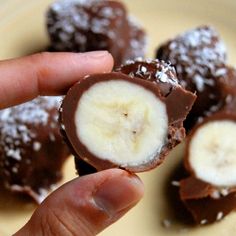 a hand holding a half eaten banana on top of a white plate filled with chocolate