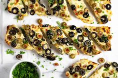 several slices of pizza with olives and parsley next to a bowl of pesto