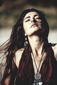 a woman with her eyes closed wearing earrings and a brown top is looking up at the sky